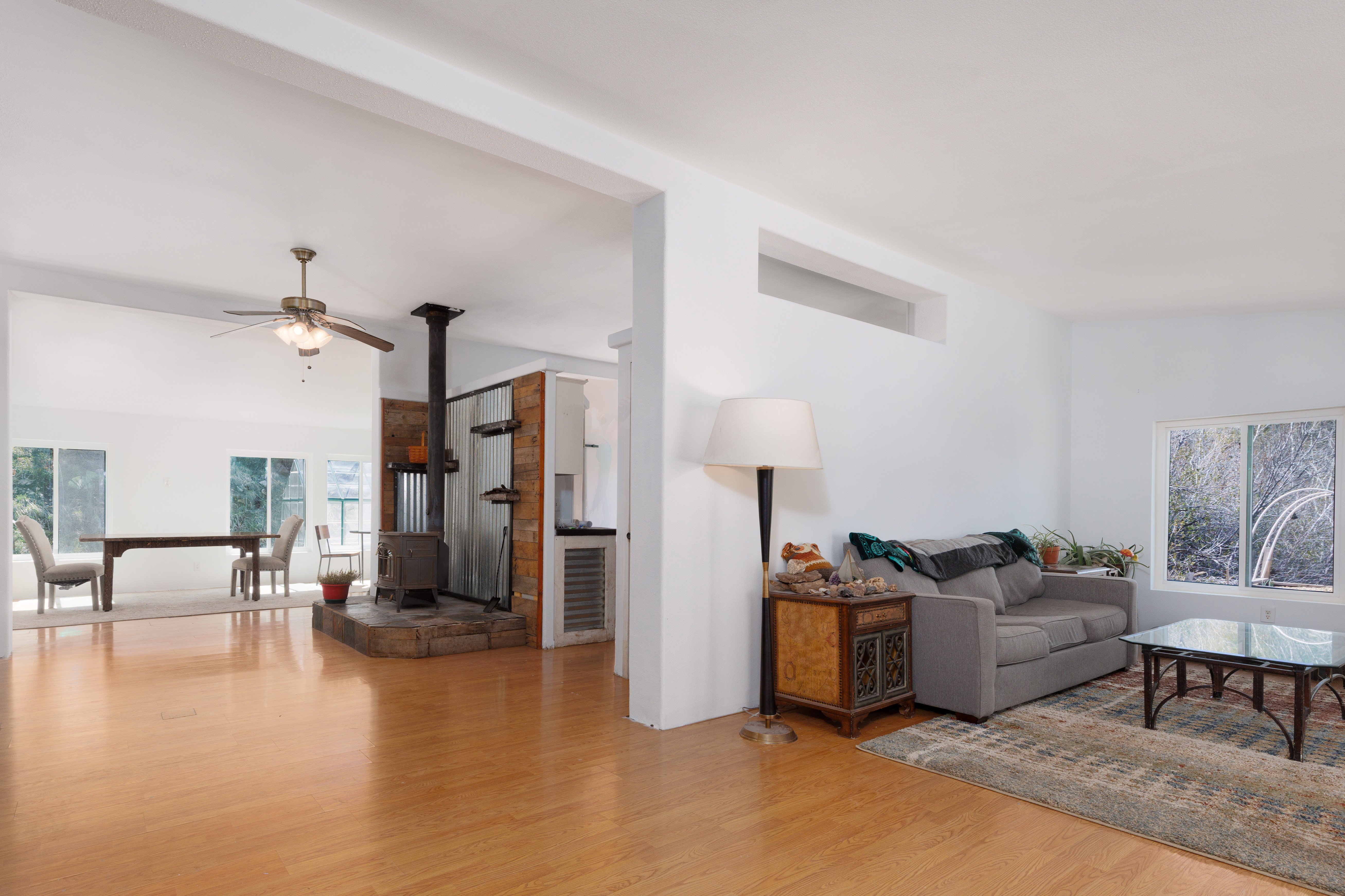 Living area featuring a wood stove, light wood-style floors, ceiling fan, and healthy amount of natural light