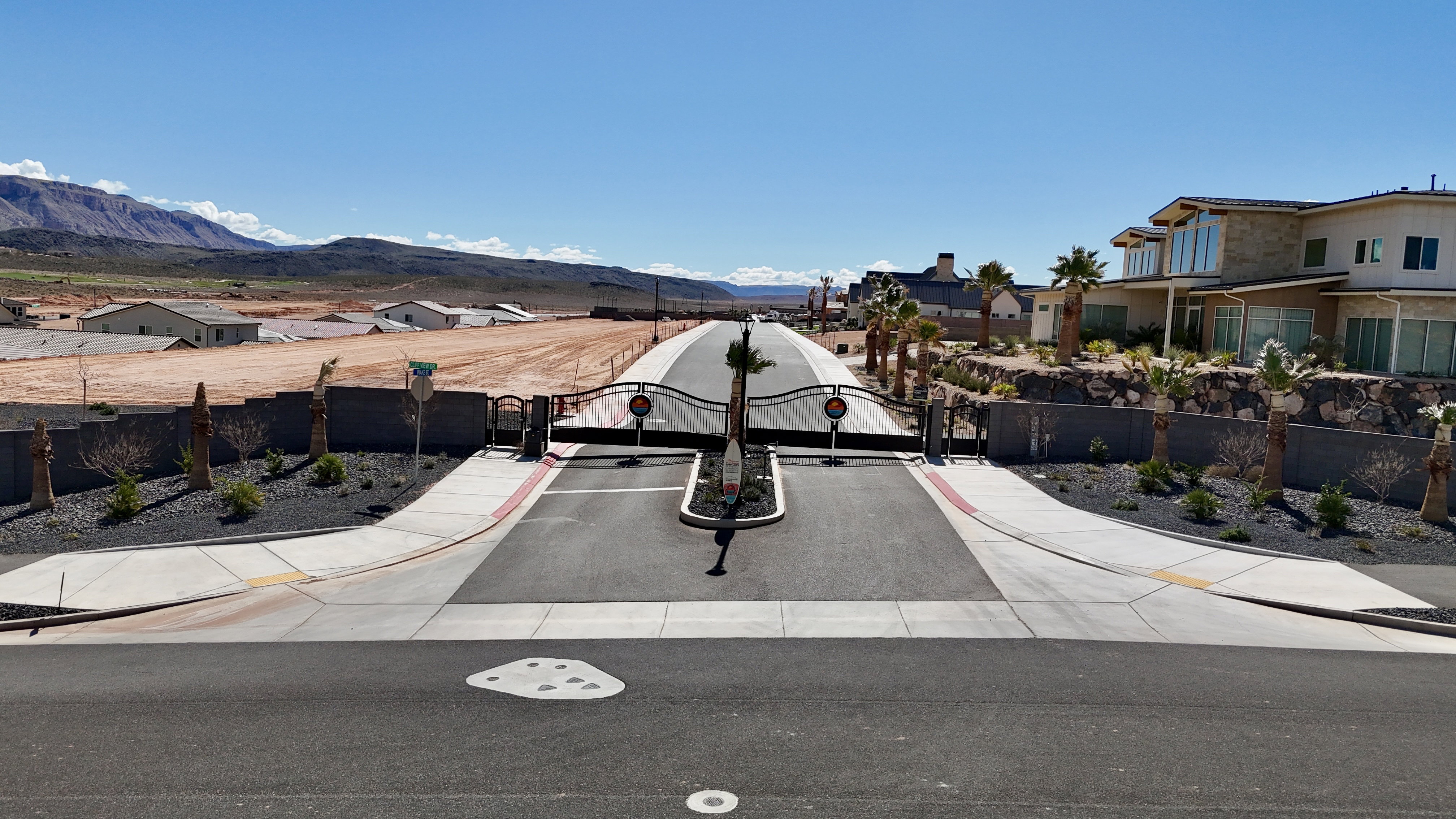 View of asphalt road with sidewalks, a gated entry, a gate, a residential view, and a mountain view