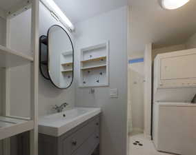 Full bathroom featuring curtained shower, stacked washer / drying machine, and vanity