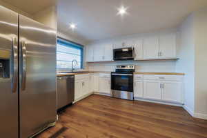 Kitchen featuring stainless steel appliances, white cabinets, light countertops, and dark wood-style flooring