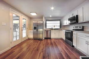 Kitchen with stainless steel appliances, white cabinets, light countertops, and dark wood-type flooring