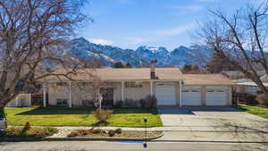 View of front of house featuring a garage, brick siding, a mountain view, a chimney, and driveway