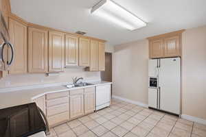 Kitchen featuring light wood finish cabinets, appliances, light countertops, and light tile flooring