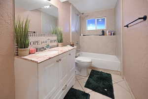 Bathroom with a textured wall, vanity, bathtub / shower combination, light tile patterned flooring, and backsplash
