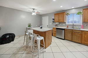Kitchen featuring wood finish cabinets, light countertops, dishwasher, a kitchen island, and light tile patterned floors