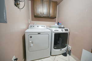 Laundry room with cabinet space, washing machine and clothes dryer, light tile patterned floors, and a textured wall