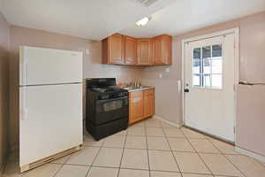 Kitchen featuring freestanding refrigerator, gas stove, light countertops, light tile patterned floors, and wood finish cabinetry