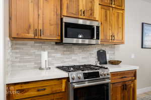 Kitchen featuring stainless steel appliances, light stone counters, tasteful backsplash, and wood finish cabinetry