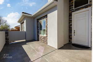 Property entrance with stone siding, stucco siding, and a patio area