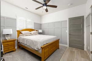 Bedroom with a decorative wall, light wood-type flooring, ceiling fan, and wainscoting