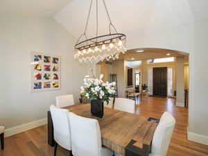 Dining space with arched walkways, wood finished floors, lofted ceiling, and a chandelier