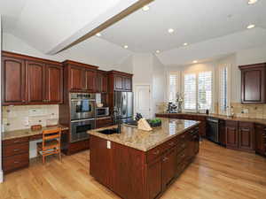 Kitchen featuring tasteful backsplash, lofted ceiling, a kitchen island with sink, stainless steel appliances, and light stone counters