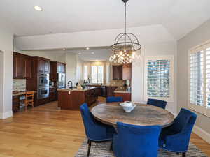 Dining space with vaulted ceiling, light wood-style floors, and suspended lighting