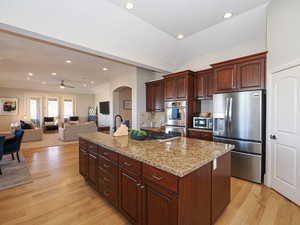 Kitchen featuring a center island, stainless steel appliances, open floor plan, light stone countertops, and light wood finished floors