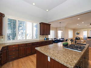Kitchen with open floor plan, light wood finished floors, dark wood finish cabinets, backsplash, and a center island with sink
