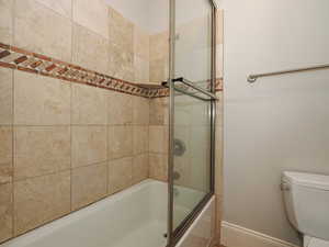Bathroom featuring toilet and combined bath / shower with glass door