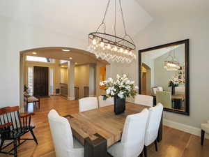 Dining space with arched walkways, a chandelier, wood finished floors, and vaulted ceiling
