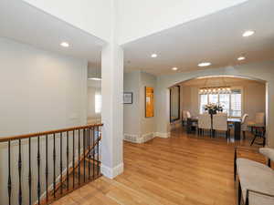 Hall with light wood finished floors, arched walkways, plenty of natural light, and recessed lighting