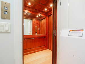 Elevator featuring wood finished floors, recessed lighting, ornamental molding, and wooden walls