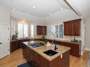Kitchen with a center island with sink, light wood-style floors, light stone countertops, backsplash, and recessed lighting