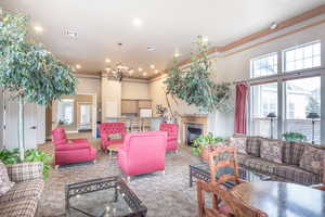 Living room featuring a fireplace, a high ceiling, suspended lighting, carpet flooring, and crown molding
