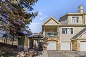View of front of home with a balcony, a garage, driveway, and stone siding