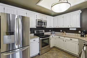 Kitchen featuring stainless steel appliances, white cabinets, and light stone counters
