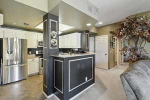Kitchen featuring stainless steel appliances, white cabinetry, light stone counters, recessed lighting, and dark carpet