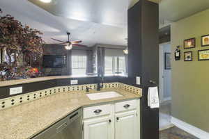 Kitchen with light stone counters, dishwasher, a ceiling fan, and white cabinets