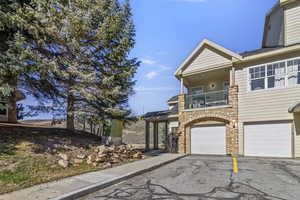 View of front of home featuring a balcony, asphalt driveway, an attached garage, and stone siding