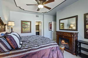 Bedroom featuring ceiling fan, light colored carpet, connected bathroom, and a lit fireplace
