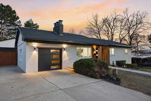 View of front of property featuring a chimney, a garage, brick siding, driveway, and roof with shingles
