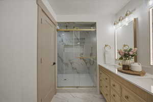 Full ensuite bath featuring double vanity, a marble finish shower, and light marble finish flooring