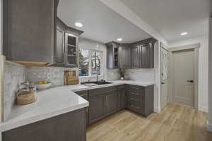 Kitchen featuring glass fronted cabinets, light wood-type flooring, tasteful backsplash, dark wood finish cabinetry, and recessed lighting