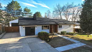 View of front facade featuring brick siding, a chimney, driveway, and a shingled roof