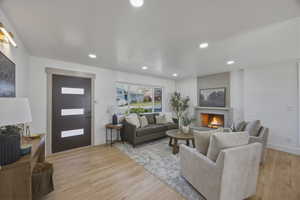 Living area with light wood finished floors, a warm lit fireplace, and recessed lighting