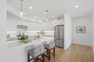 Kitchen with a breakfast bar, white cabinets, stainless steel appliances, pendant lighting, and light wood-type flooring