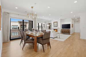 Dining area featuring a warm lit fireplace, light wood-style flooring, and hanging lights
