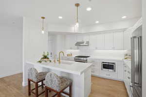 Kitchen featuring a breakfast bar area, white cabinets, high end appliances, and light wood-style flooring