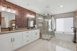 Primary Bathroom featuring a stall shower, a freestanding bath, double vanity, recessed lighting, and tile walls