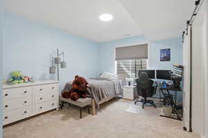 Bedroom featuring a barn door, an office area, and light carpet