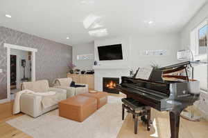 Living room with light wood finished floors, a brick fireplace, wallpapered walls, recessed lighting, and an accent wall