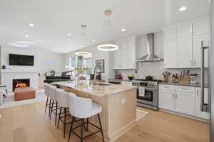 Dual tone kitchen with open floor plan, dark stone countertops, light wood-style floors, stainless steel range with gas stovetop, and a kitchen bar
