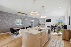 Kitchen with light wood finish cabinetry, a kitchen island with sink, light stone counters, wallpapered walls, and hanging light fixtures
