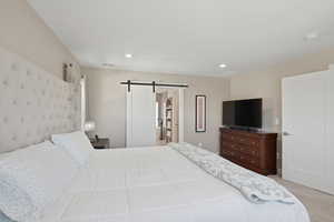 Primary Bedroom with a barn door, light colored carpet, and recessed lighting