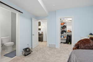 Bedroom with ensuite bathroom, a spacious closet, light carpet, and a barn door
