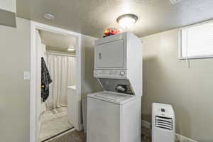 Laundry area featuring stacked washing machine and dryer, a textured ceiling, and light marble finish flooring
