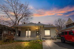 View of front of house with brick siding, covered porch, a chimney, and a yard