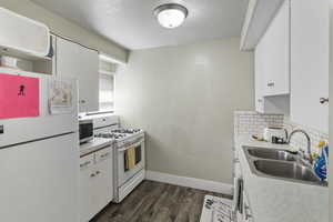 Kitchen with white cabinetry, white appliances, light countertops, a textured ceiling, and dark wood-type flooring