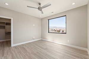 Unfurnished bedroom with a spacious closet, recessed lighting, a ceiling fan, and light wood-type flooring